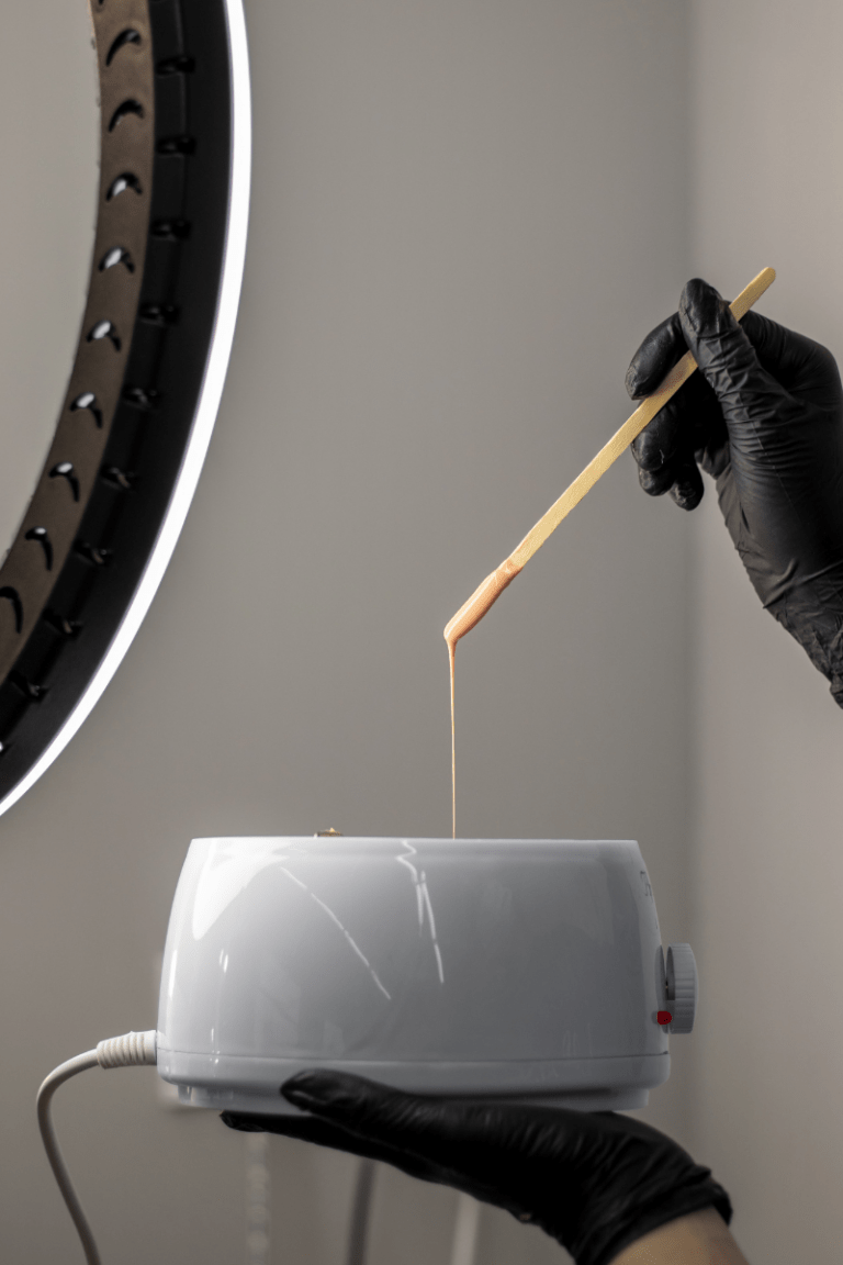 Hand in black gloves holding a wax pot with a stick dripping wax above it