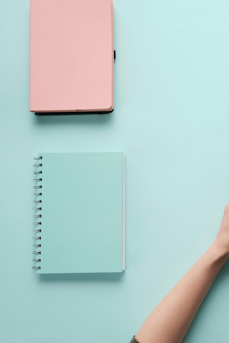 Blue background with pink and blue notebook on it and an arm in the bottom right hand corner