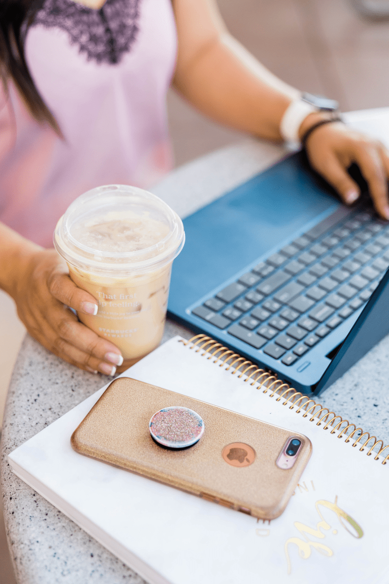 A woman typing on a laptop while holding a coffee