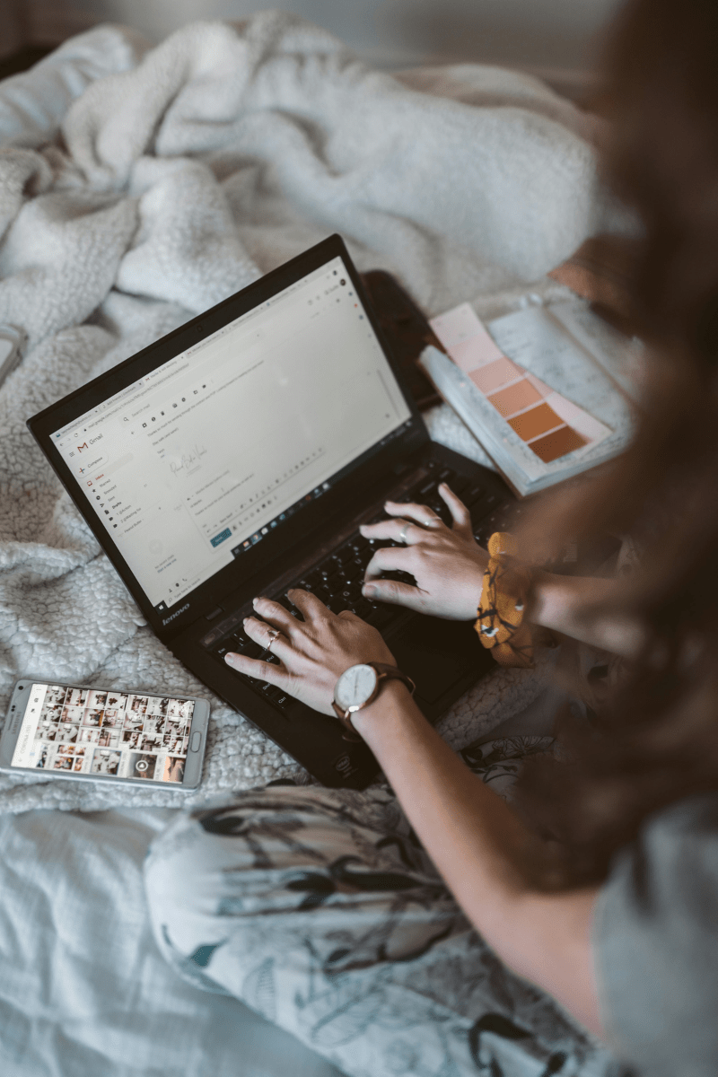 A woman typing on her laptop sitting on a blanket