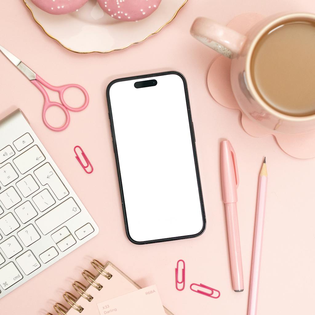 Modern pink-themed desk setup with smartphone, keyboard, and coffee cup.